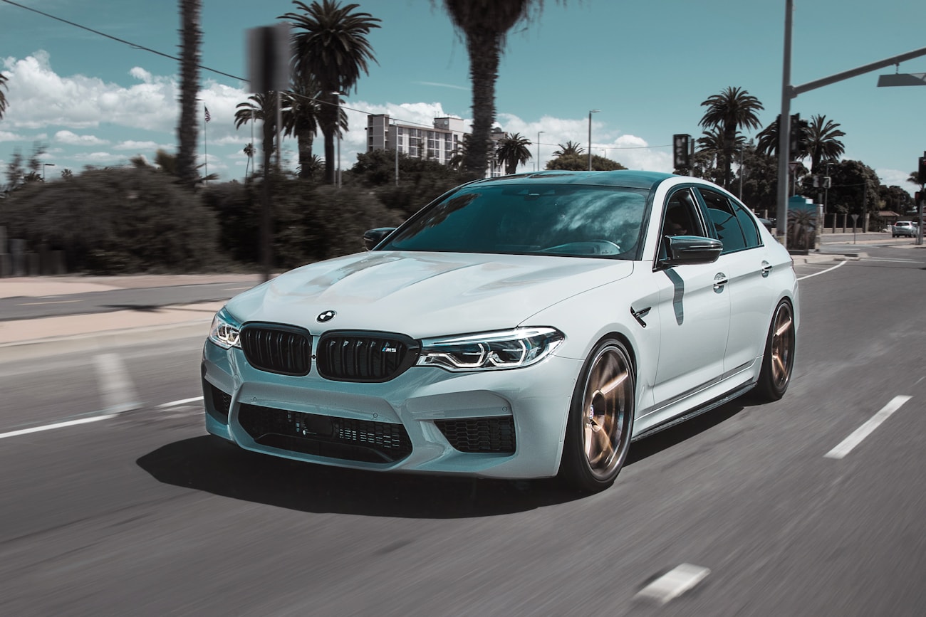 Светлый BMW M5 Competition в движении на городской набережной