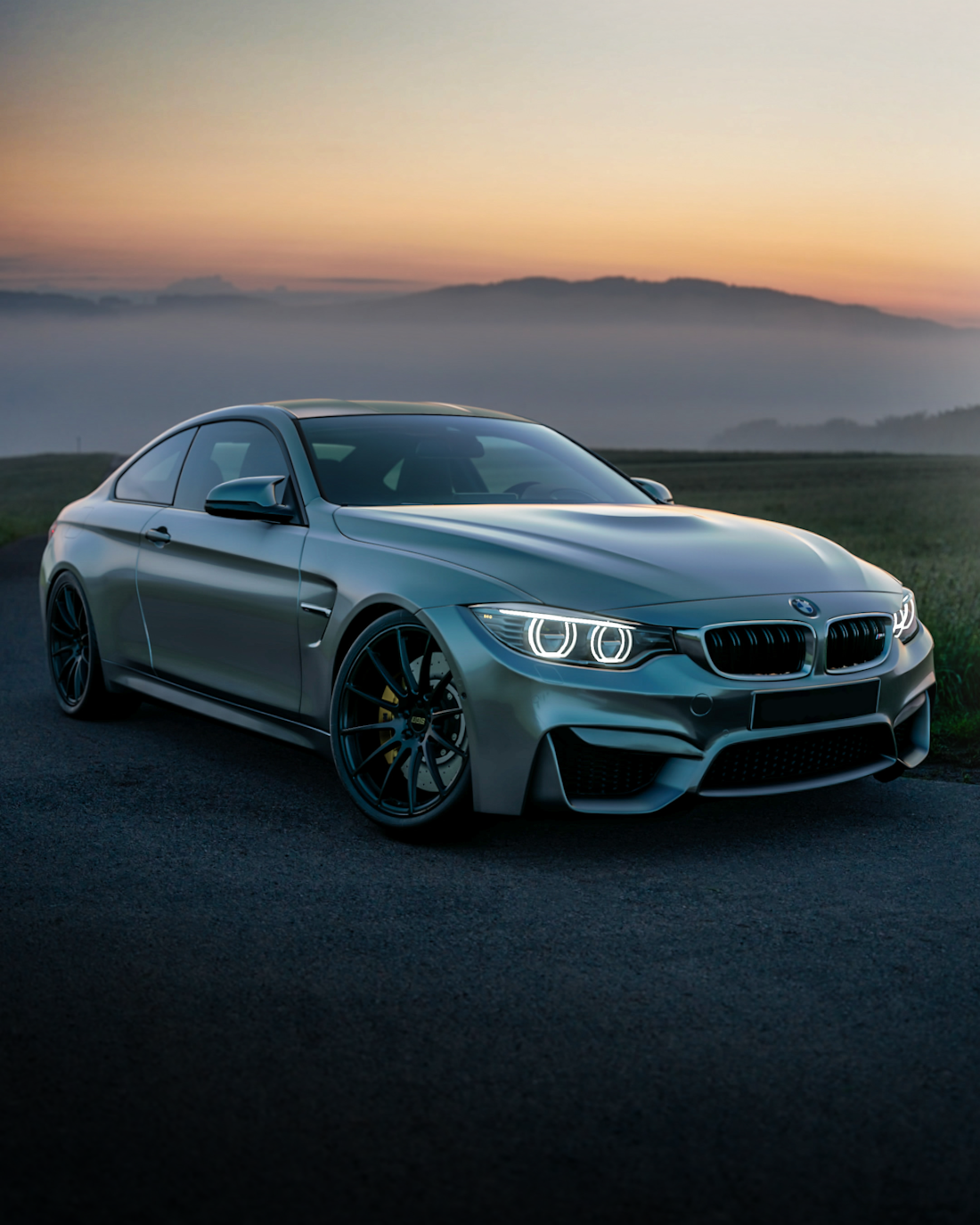 BMW M4 на фоне тумана и заката — свет фар растворяется в сумерках